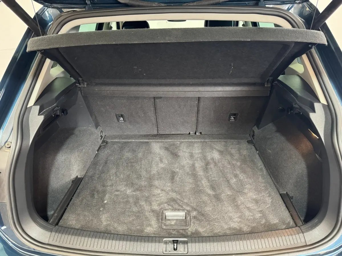 Coffre ouvert vu de l'arrière d'un Volkswagen Tiguan bleu 2021, avec cache-bagages relevé et intérieur noir.