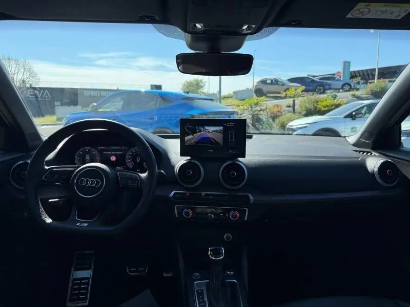 Vue intérieure avant de l'Audi Q2 35 TDI S line 2025, avec tableau de bord noir et écran central affichant la caméra de recul.