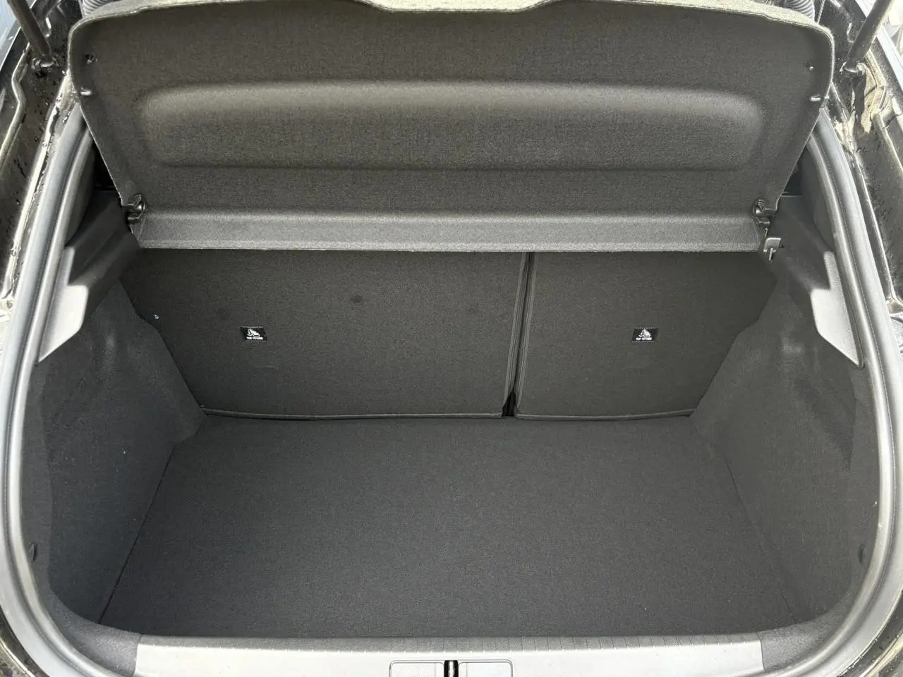 Coffre ouvert vu de l'arrière d'une Peugeot 208 Hybrid 110 e-DSC6 GT noir Perla, intérieur entièrement noir.