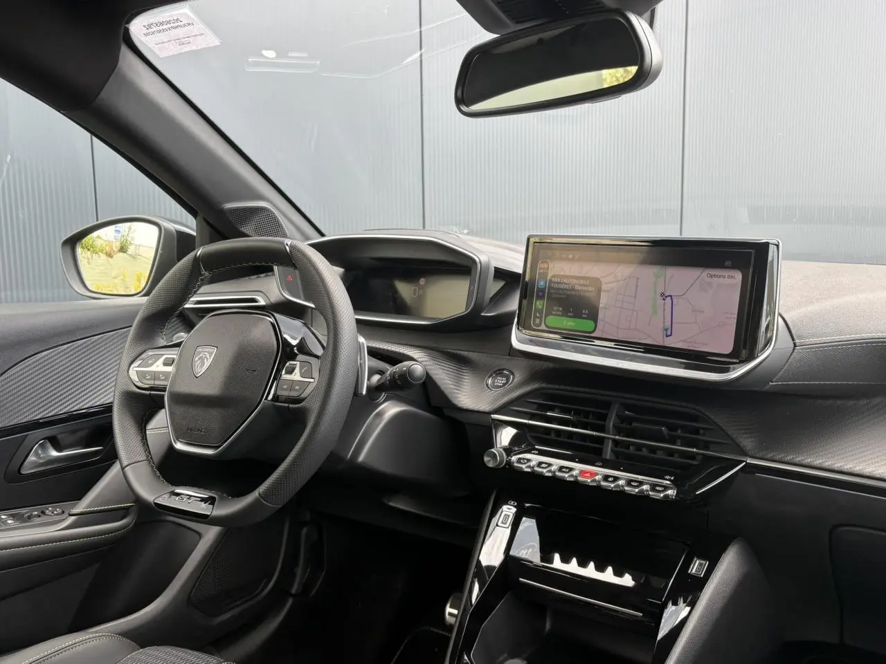 Vue intérieure côté conducteur du Peugeot 208 Hybrid 110 GT 2025, avec tableau de bord numérique et écran tactile central.