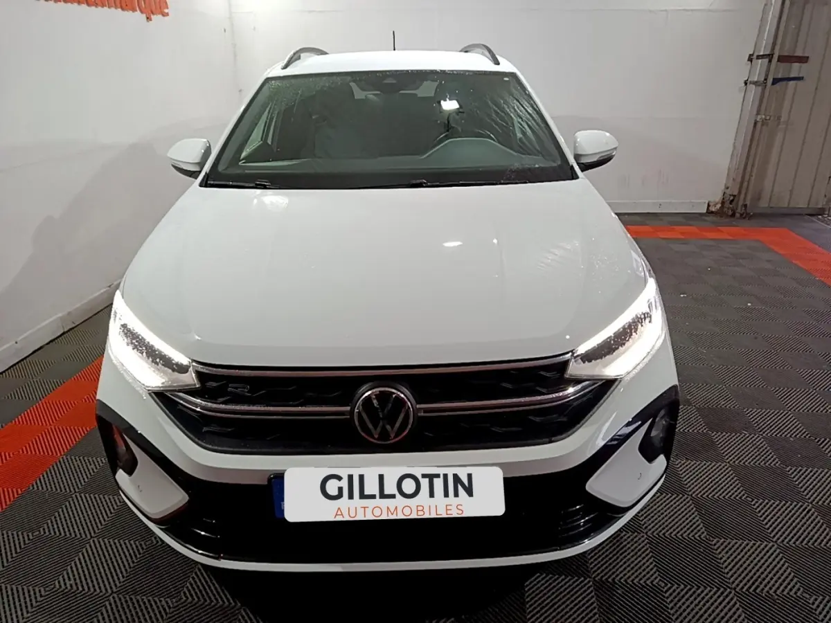 Vue frontale d'un Volkswagen Taigo blanc avec phares LED allumés et calandre R-Line dans un showroom.