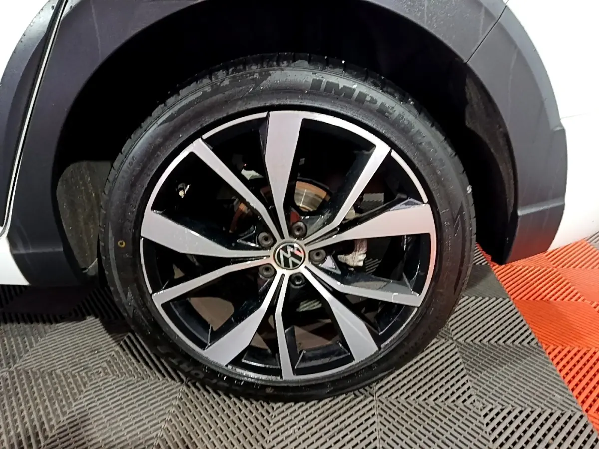 Gros plan sur la roue avant droite d’un Volkswagen Taigo blanc, jante alliage bicolore noir et argent.