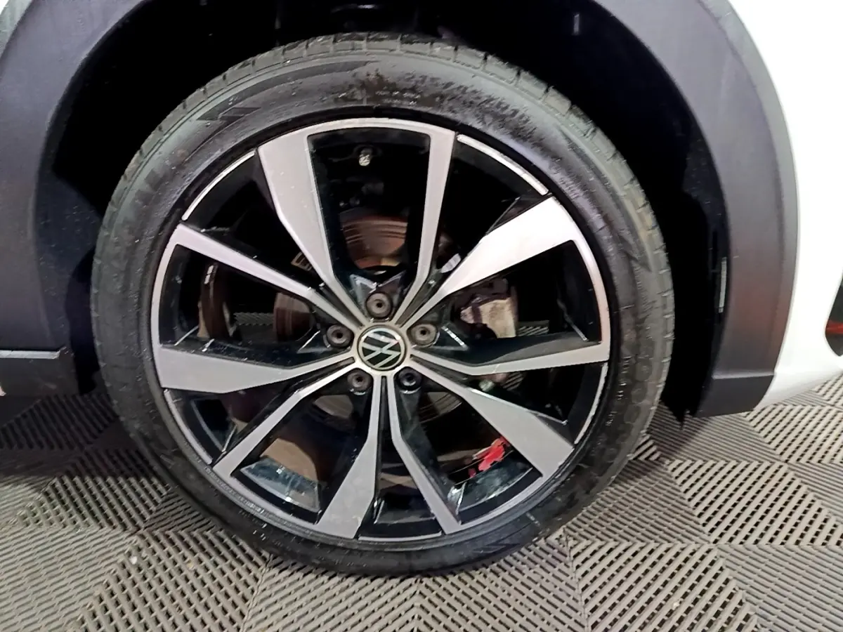 Gros plan sur la roue avant droite du Volkswagen Taigo blanc, jante alliage noir et argentée avec logo VW central.