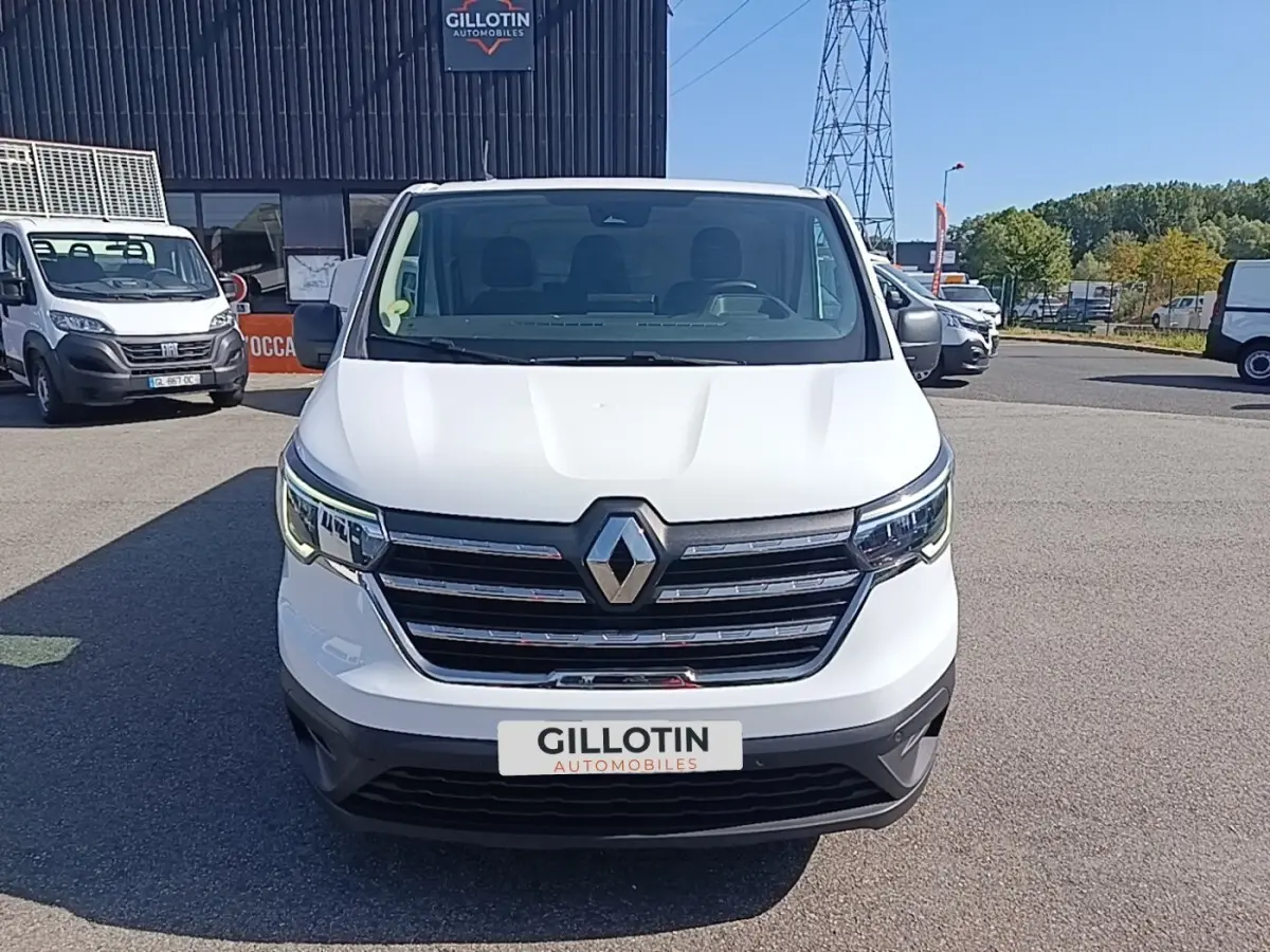 Vue avant d’un Renault Trafic Fourgon blanc 2023 avec calandre chromée et phares LED allumés.