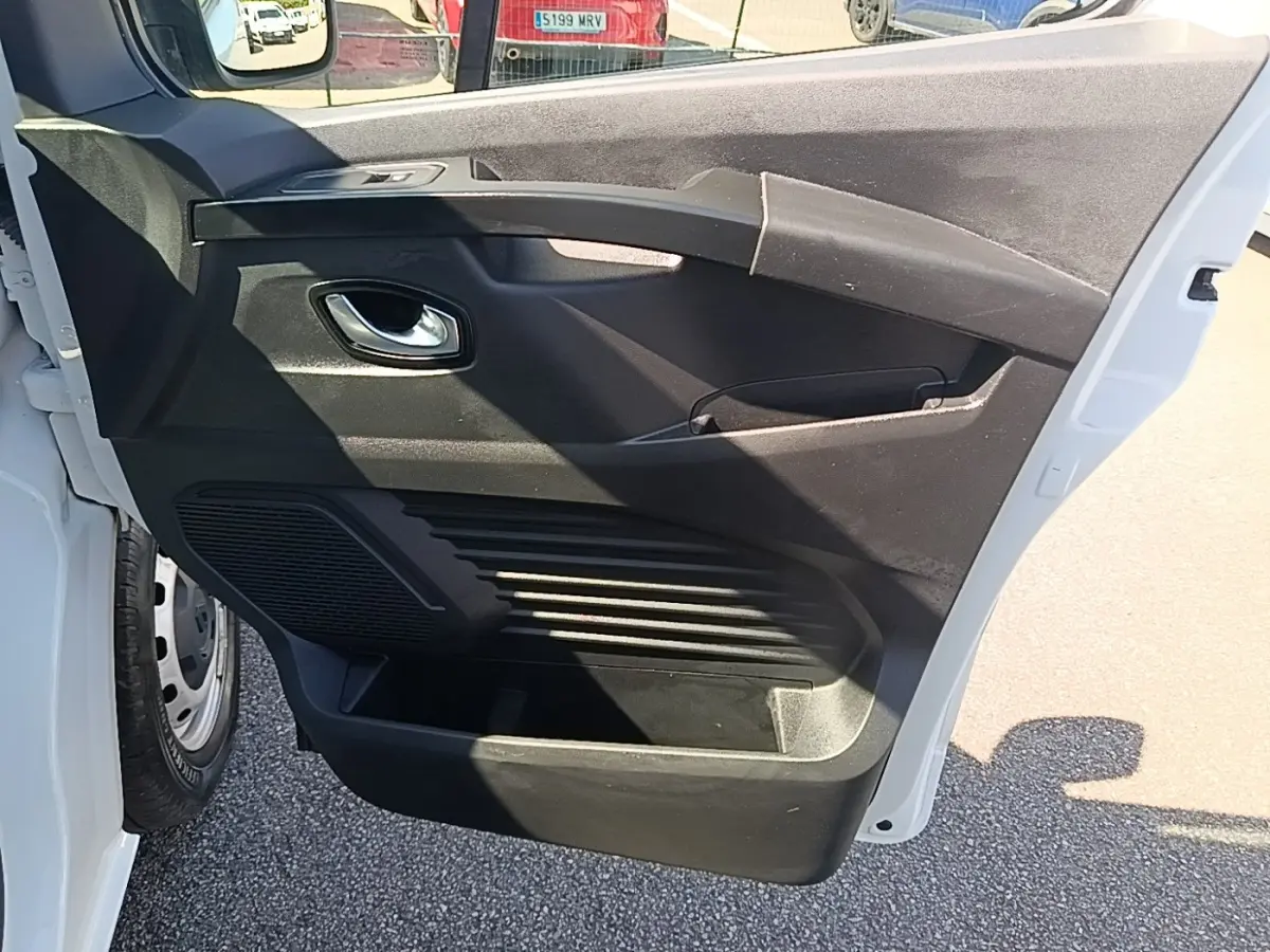 Vue rapprochée de la porte avant gauche ouverte du Renault Trafic Fourgon blanc, montrant la poignée intérieure et les rangements.