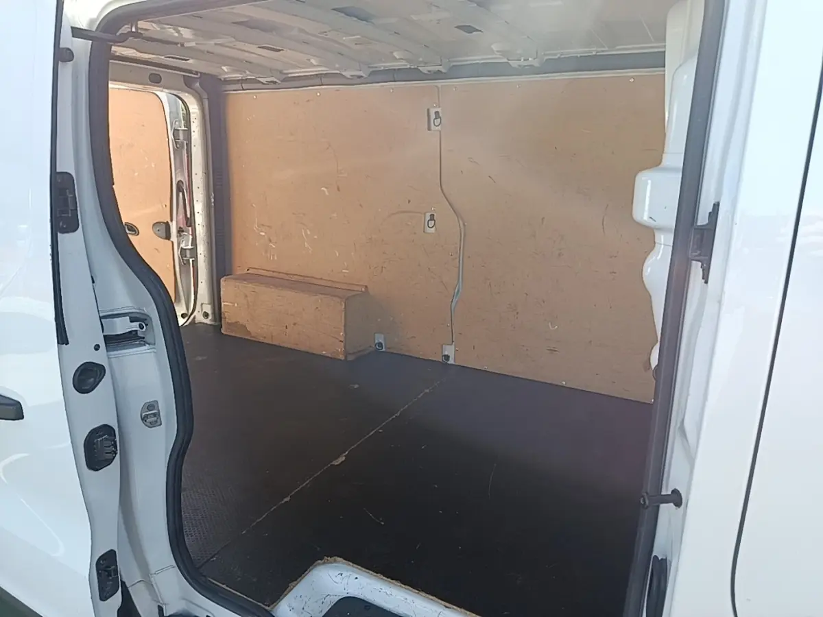 Vue intérieure côté droit du fourgon blanc Renault Trafic avec cloison bois et plancher noir antidérapant.