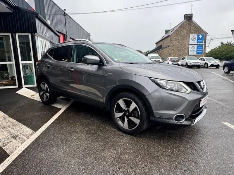 Nissan Qashqai gris Squale vu de 3/4 avant droit, avec jantes alliage et feux avant allumés par temps pluvieux.