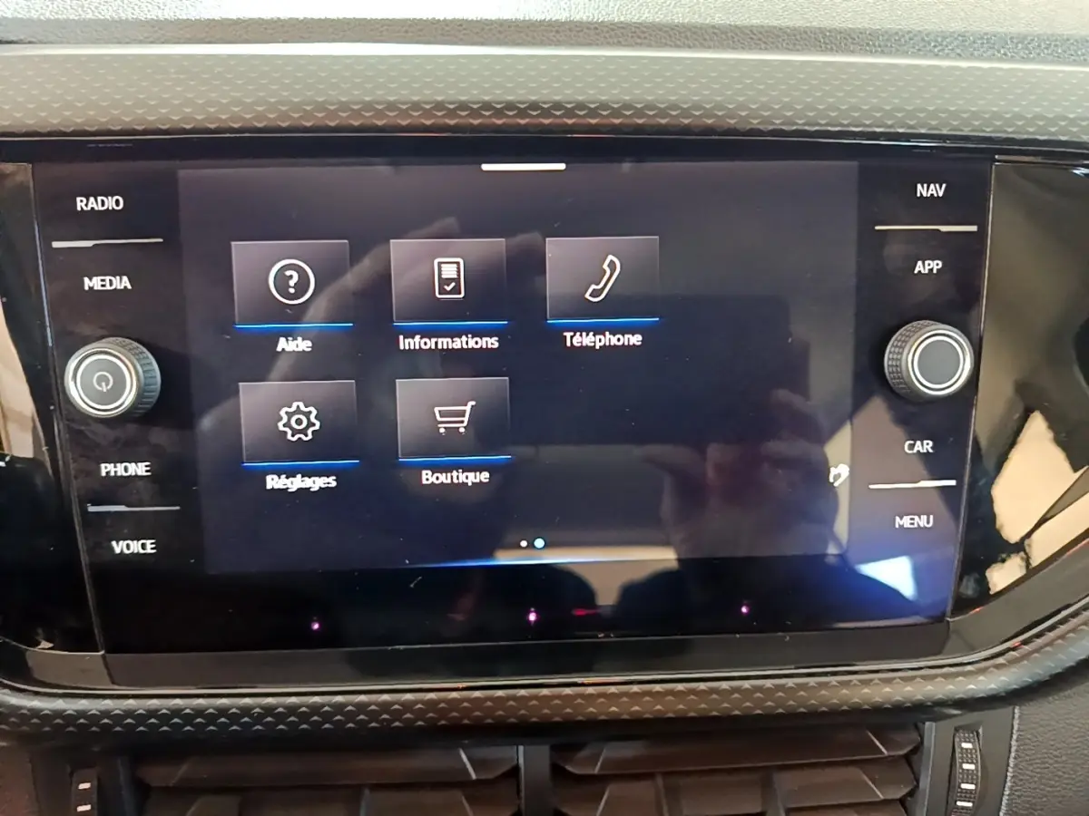 Écran tactile central du Volkswagen T-Cross gris foncé, affichant le menu principal avec options radio, téléphone et réglages.