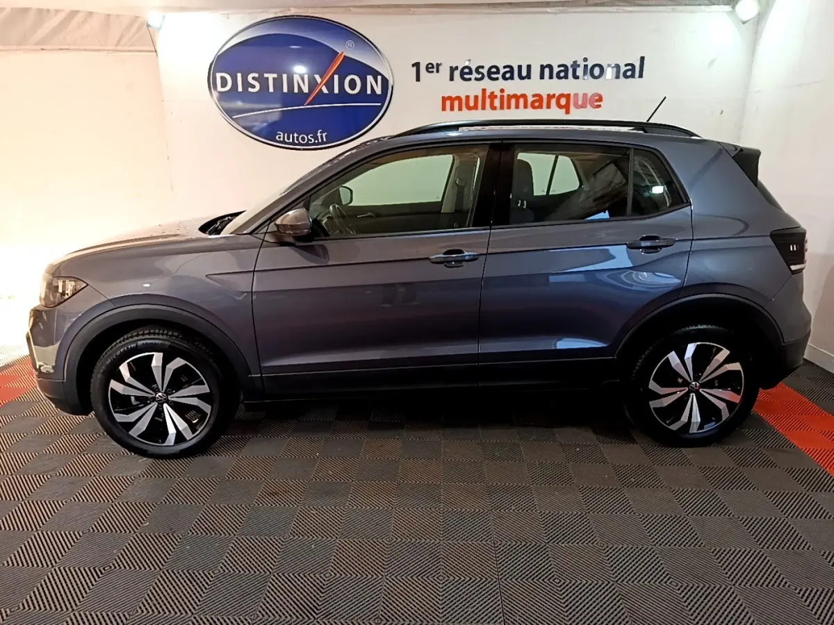 Vue de profil côté gauche d'un Volkswagen T-Cross gris foncé 2023 avec jantes alliage bicolores et barres de toit noires.