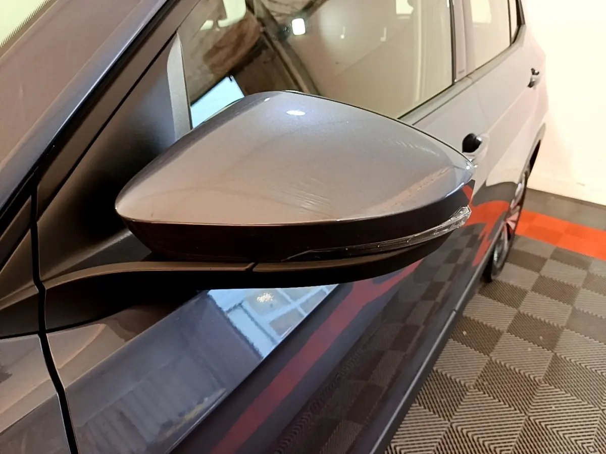 Rétroviseur côté gauche gris foncé du Volkswagen T-Cross 2023, vue rapprochée avec carrosserie et partie latérale visibles.