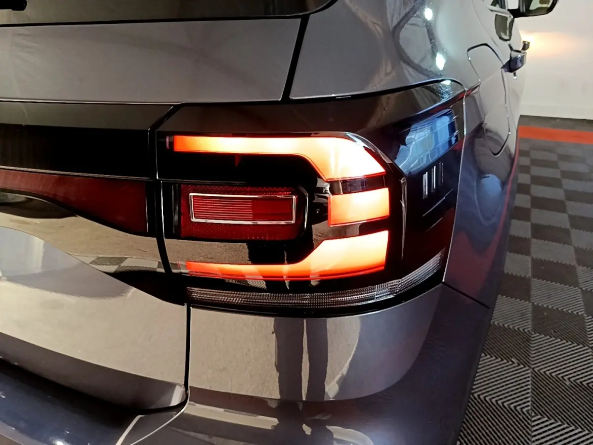 Gros plan sur le feu arrière droit allumé d’un Volkswagen T-Cross gris foncé, avec reflets sur la carrosserie.