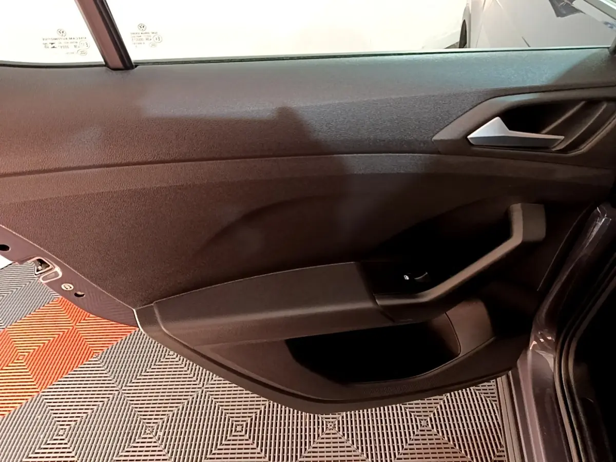 Vue intérieure de la porte avant gauche du Volkswagen T-Cross gris foncé, avec poignée et commande de vitre visible.