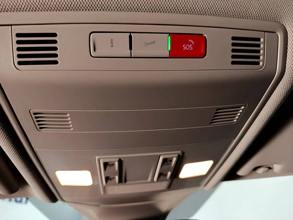 Vue en contre-plongée du panneau de commande de toit intérieur gris clair du Volkswagen T-Cross 2023 avec bouton SOS rouge éclairé.
