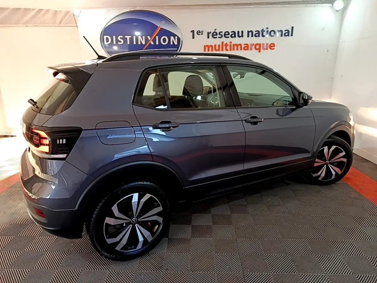Vue 3/4 arrière droite d'un Volkswagen T-Cross gris foncé avec jantes alliage et feux LED, en intérieur showroom.