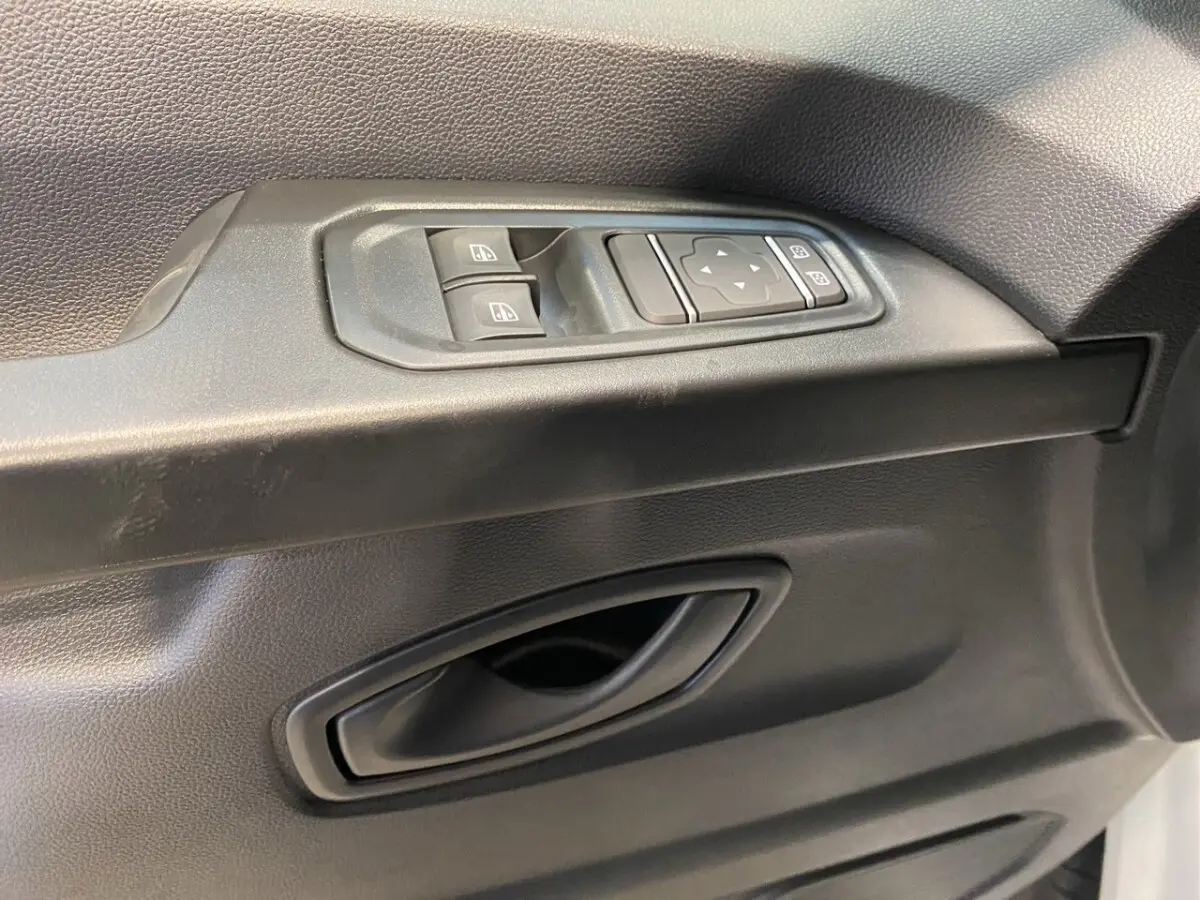Gros plan sur la commande des vitres électriques et le bouton de réglage des rétroviseurs côté conducteur d’un Renault Trafic blanc.