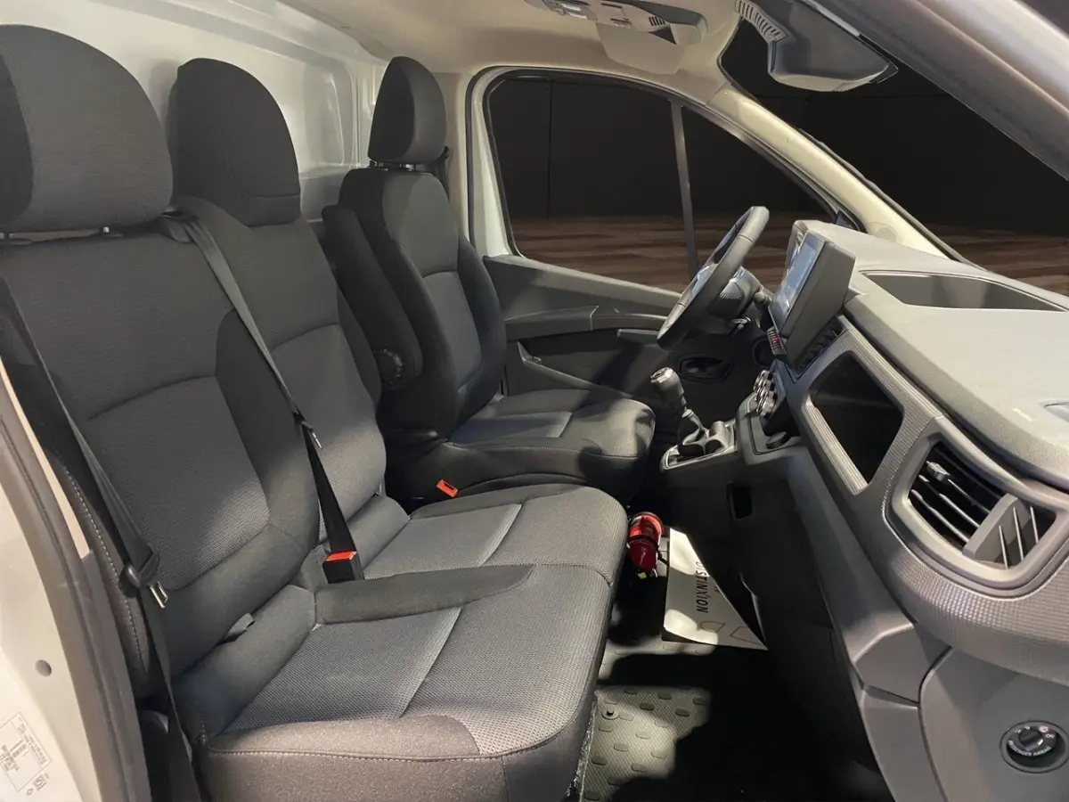 Vue intérieure côté droit du Renault Trafic Fourgon blanc, montrant les sièges avant et le tableau de bord avec volant multifonctions.