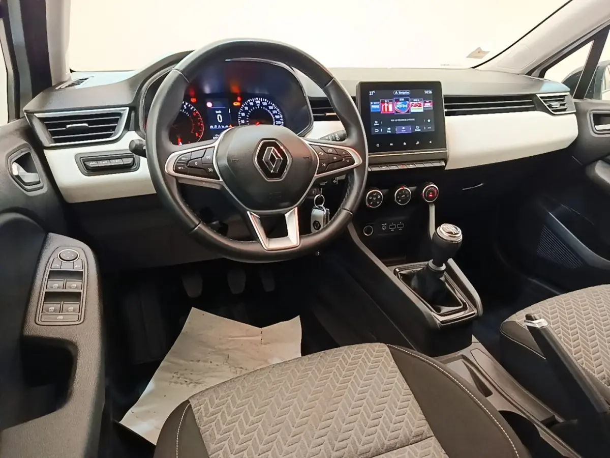 Vue intérieure avant de la Renault Clio blanche 2023, volant cuir multifonctions et écran tactile central visible.