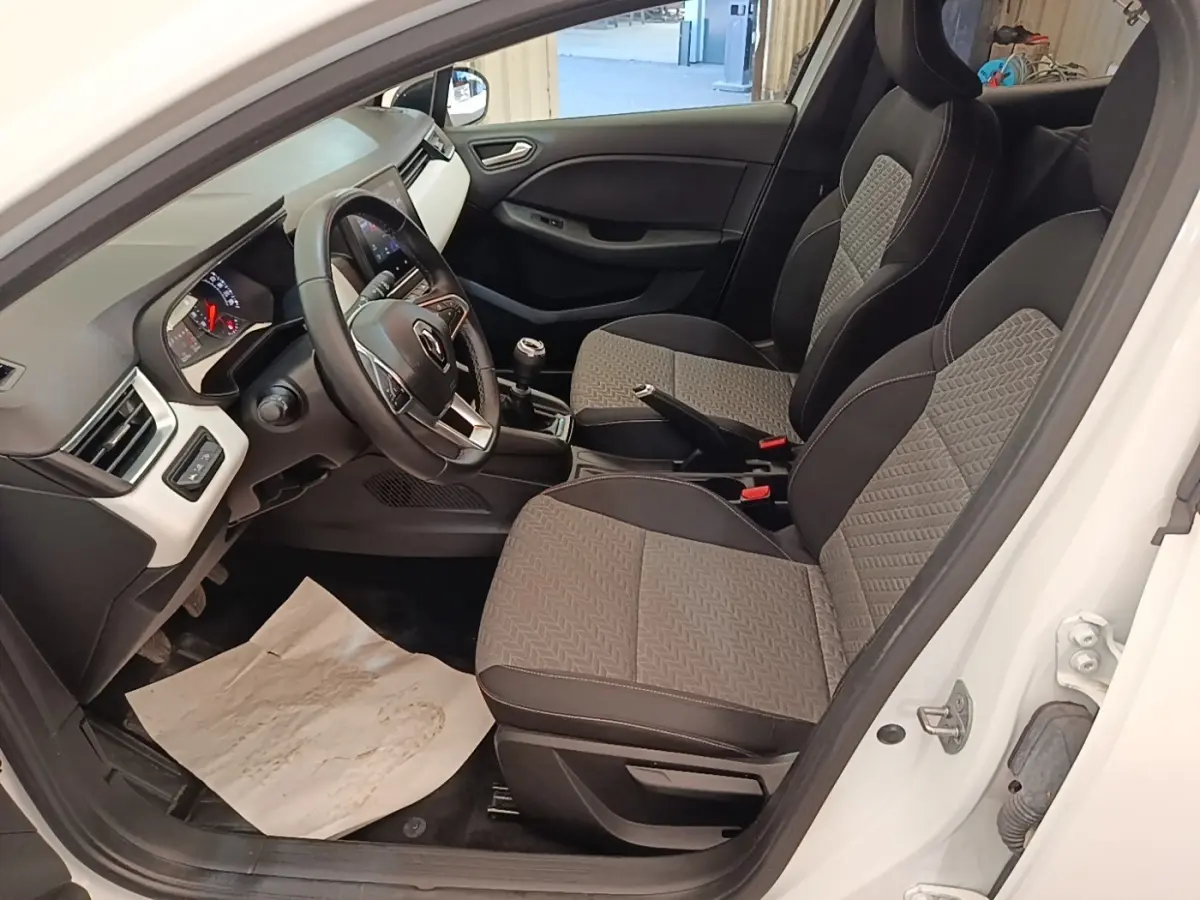 Intérieur avant droit de la Renault Clio blanche 2023, montrant sièges tissu bicolore et volant multifonctions cuir synthétique.