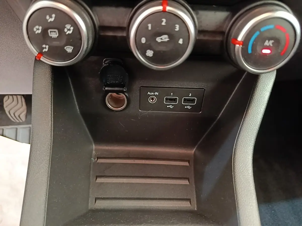Vue rapprochée de la console centrale noire de la Renault Clio avec commandes climatisation et ports USB/Aux-In.