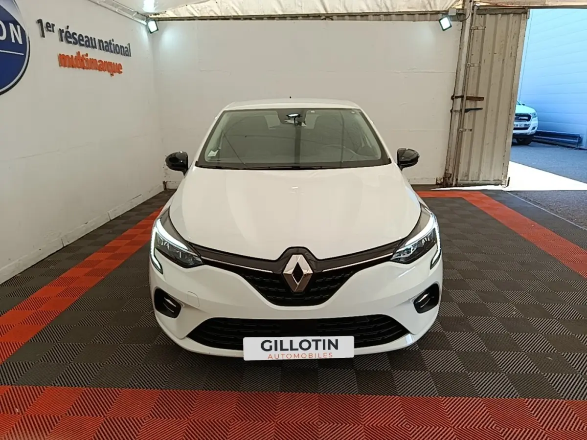 Vue avant d'une Renault Clio blanche 2023 avec phares LED allumés dans un showroom intérieur.
