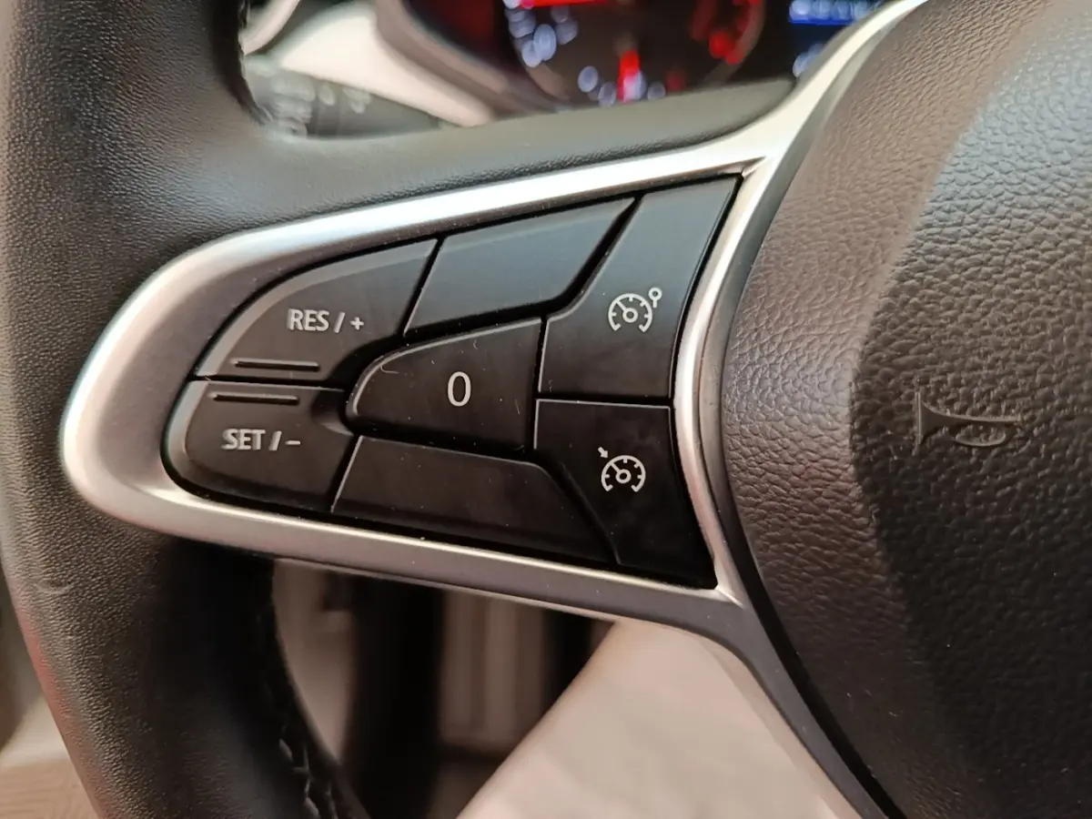 Gros plan sur les commandes du régulateur de vitesse au volant cuir synthétique d'une Renault Clio blanche 2023.
