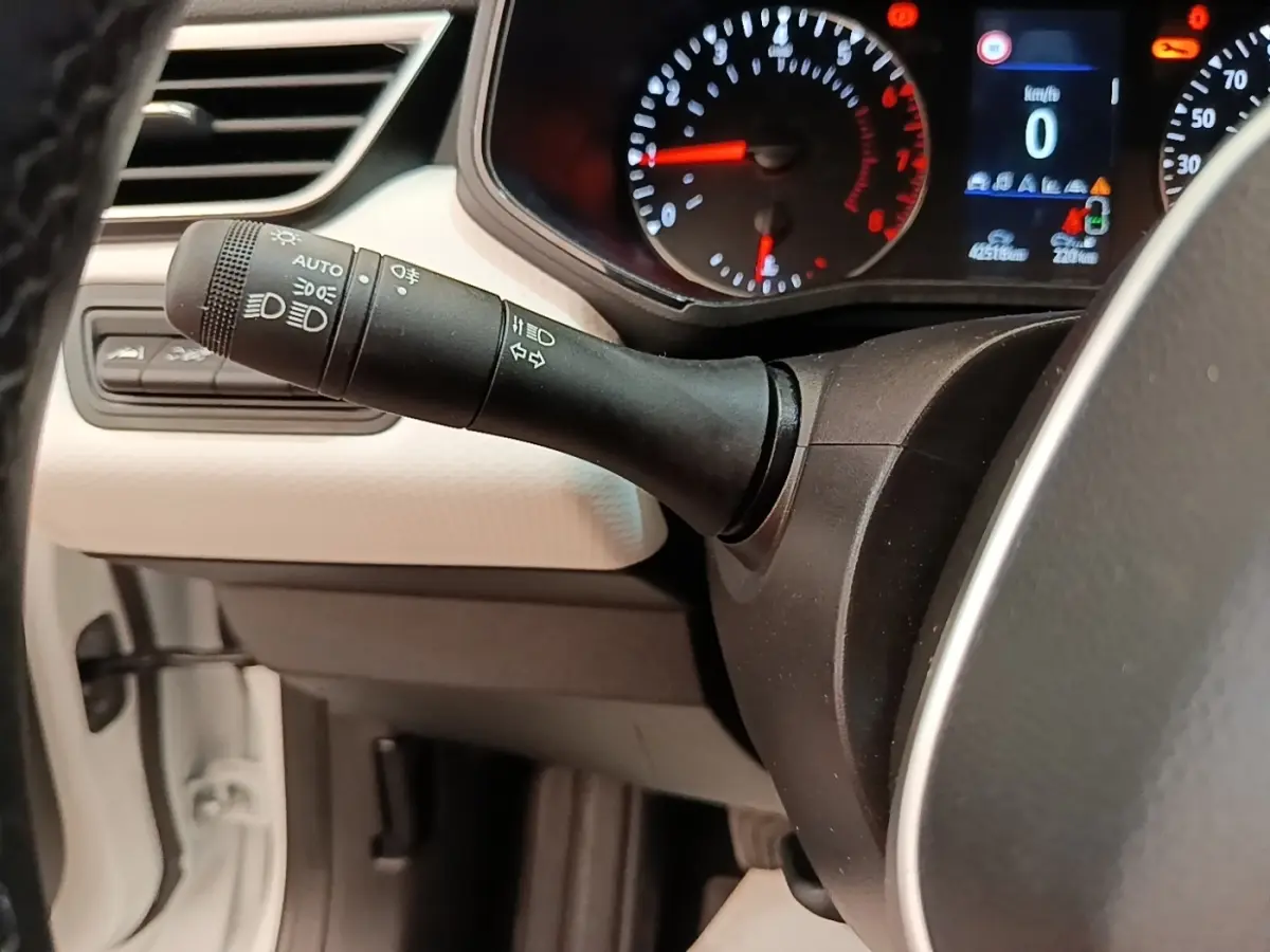 Gros plan sur la manette de commandes des phares et clignotants côté gauche du tableau de bord blanc de la Renault Clio 2023.