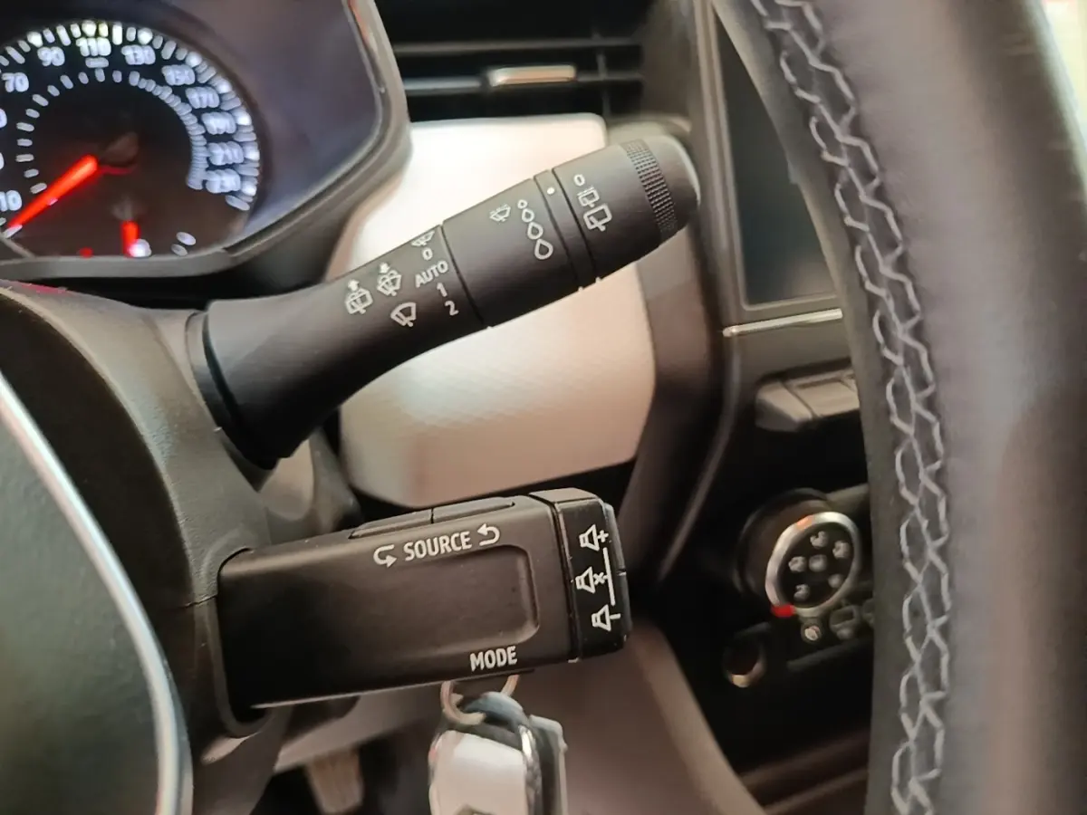 Gros plan sur les commandes au volant cuir synthétique de la Renault Clio 2023, avec tableau de bord partiellement visible.