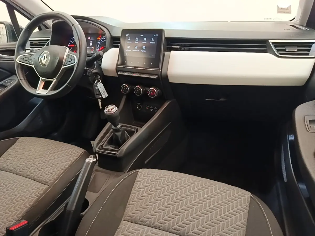 Intérieur de Renault Clio 2023 blanc, vue avant centrée sur tableau de bord, volant cuir et écran tactile central.