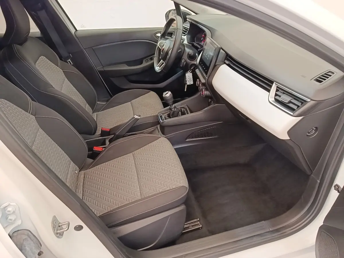 Vue intérieure côté conducteur de la Renault Clio blanche 2023, avec sièges tissu gris et tableau de bord clair.