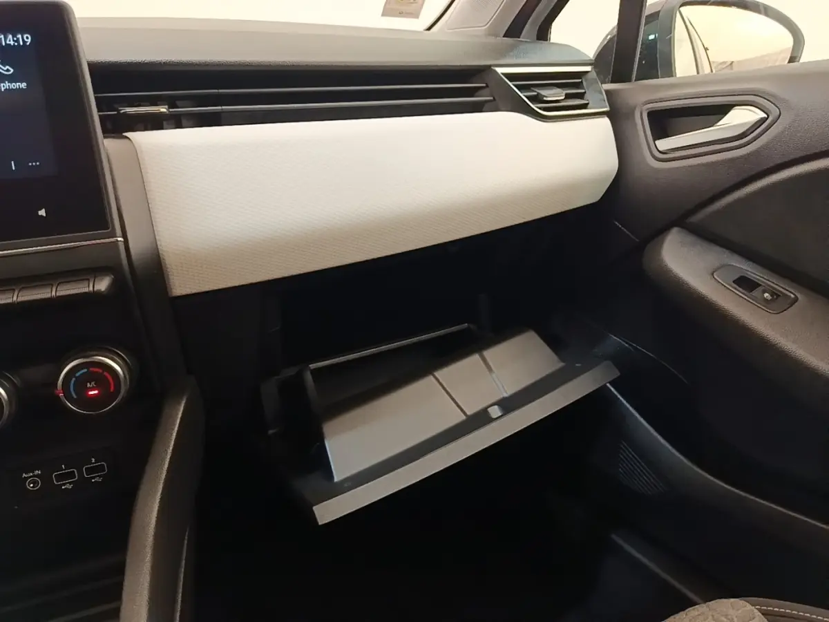 Intérieur côté passager de la Renault Clio blanc, boîte à gants ouverte et tableau de bord clair avec écran tactile.