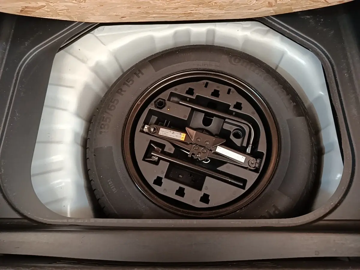 Roue de secours avec outillage intégré dans le coffre d'une Renault Clio blanche, vue de dessus.