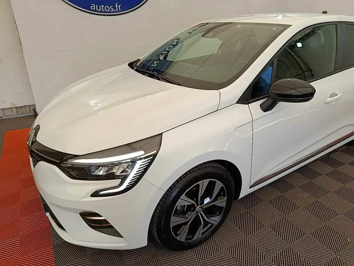 Renault Clio 2023 blanche vue 3/4 avant droit, avec phares LED et jantes alliage noires distinctives.