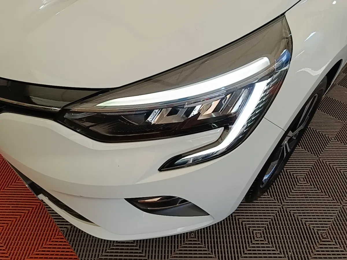 Gros plan sur le phare avant droit blanc de la Renault Clio 2023 avec éclairage LED et partie de la calandre visible.