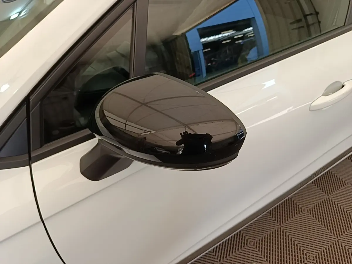 Gros plan sur le rétroviseur noir côté gauche d'une Renault Clio blanche, vue partielle de la porte avant.