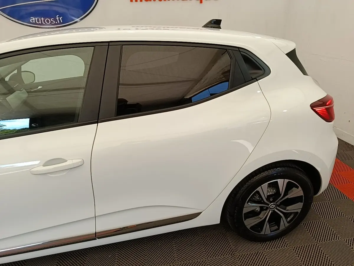 Vue latérale droite d'une Renault Clio blanche 2023 avec jantes alliage et poignées de porte intégrées.
