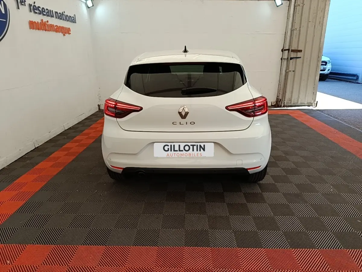 Vue arrière d'une Renault Clio blanche 2023 garée en intérieur avec feux arrière LED allumés.