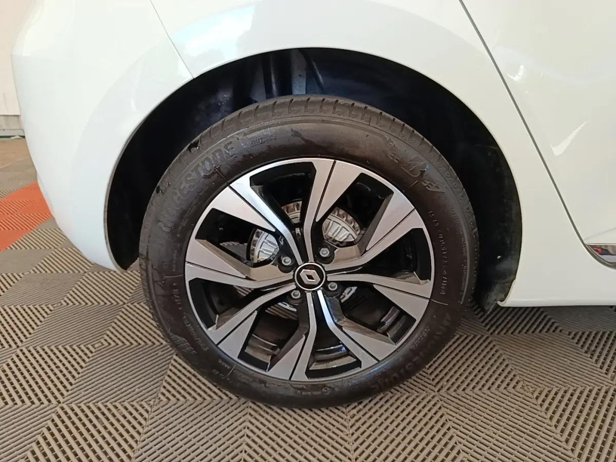 Gros plan sur la roue arrière droite d'une Renault Clio blanche, avec jante alliage bicolore et logo Renault central.