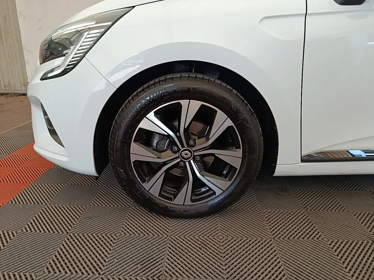 Gros plan sur la roue avant gauche d'une Renault Clio blanche 2023 avec jante alliage noire et argentée.