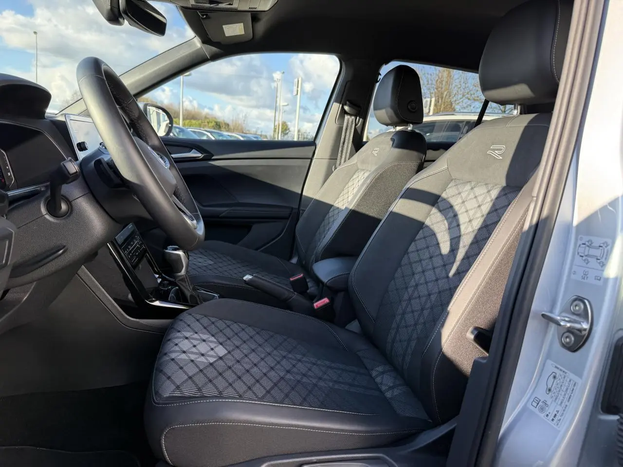 Intérieur avant droit du Volkswagen T-Cross 2025 argent, sièges R-Line en tissu noir à motifs losanges.