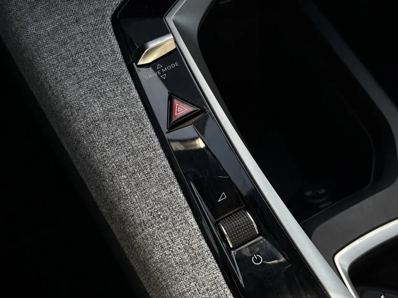 Gros plan sur la console centrale intérieure avec commandes Drive Mode et bouton warning, tissu gris et finitions noires brillantes.