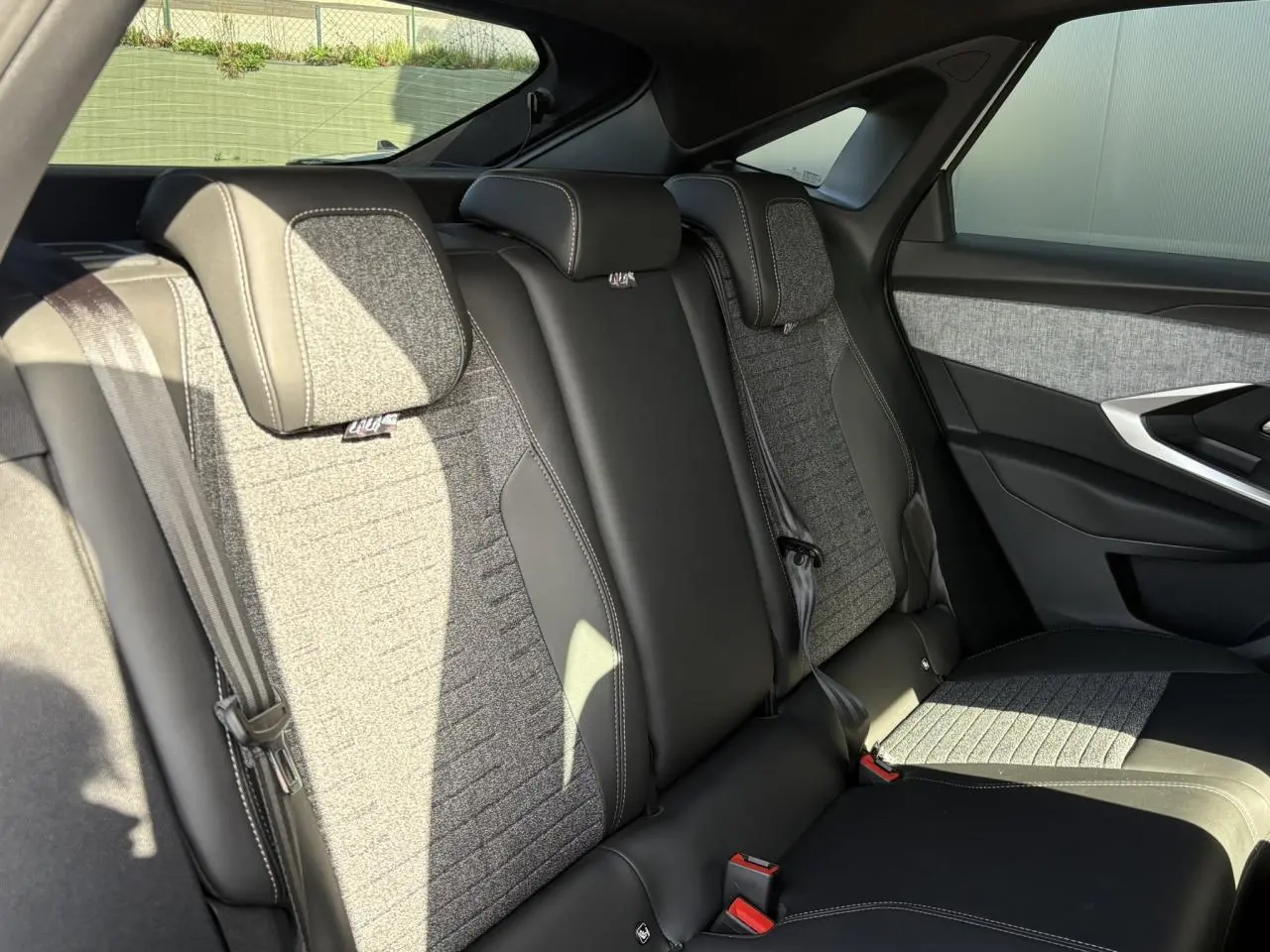 Vue latérale droite des sièges arrière gris et noirs du Peugeot 3008 Hybrid 145 e-DSC6 Allure, avec ceintures et appuie-têtes intégrés.