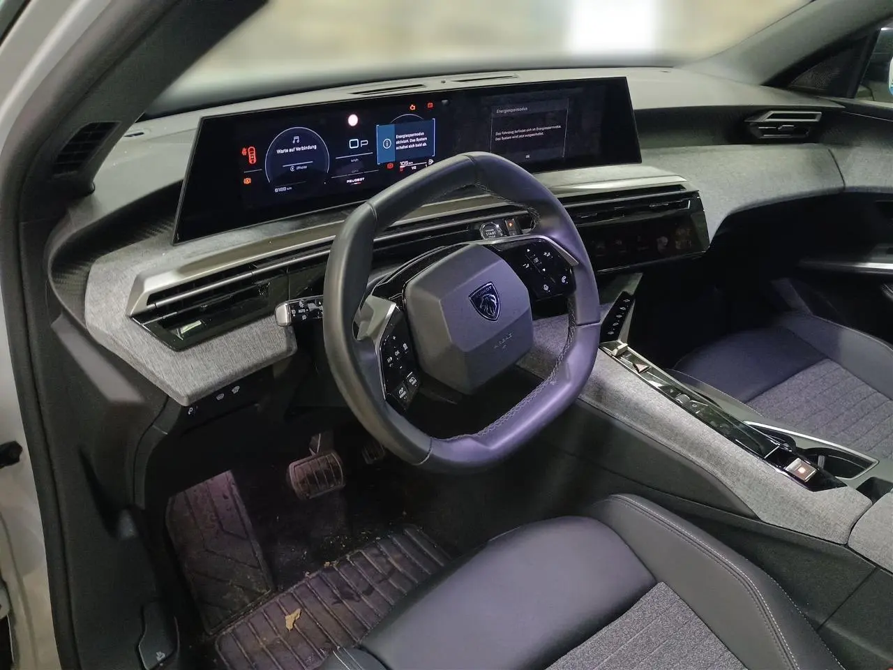 Vue intérieure du poste de conduite du Peugeot 3008 Hybrid 2025, volant compact cuir et écran panoramique 21 pouces affichant la navigation.