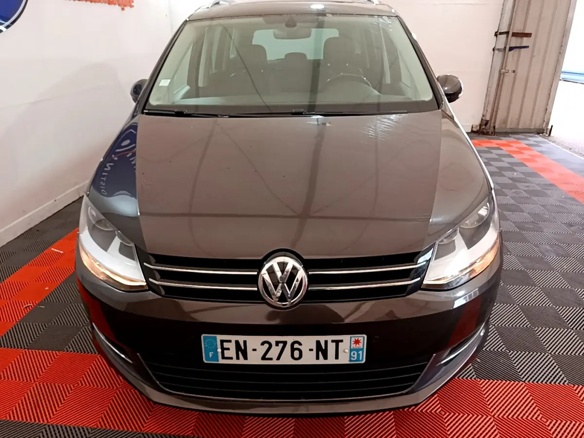 Vue frontale d'un Volkswagen Sharan marron 2017 avec calandre chromée et phares allumés en intérieur.