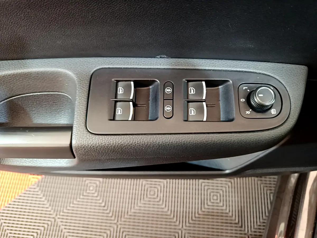 Gros plan sur les commandes de lève-vitres et réglage des rétroviseurs côté conducteur d’un Volkswagen Sharan marron.