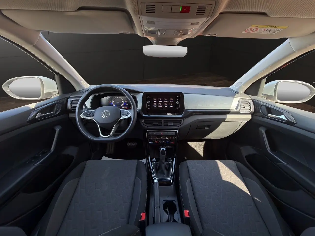 Vue intérieure avant du Volkswagen T-Cross 2025 avec tableau de bord noir et sièges tissu Life gris foncé.
