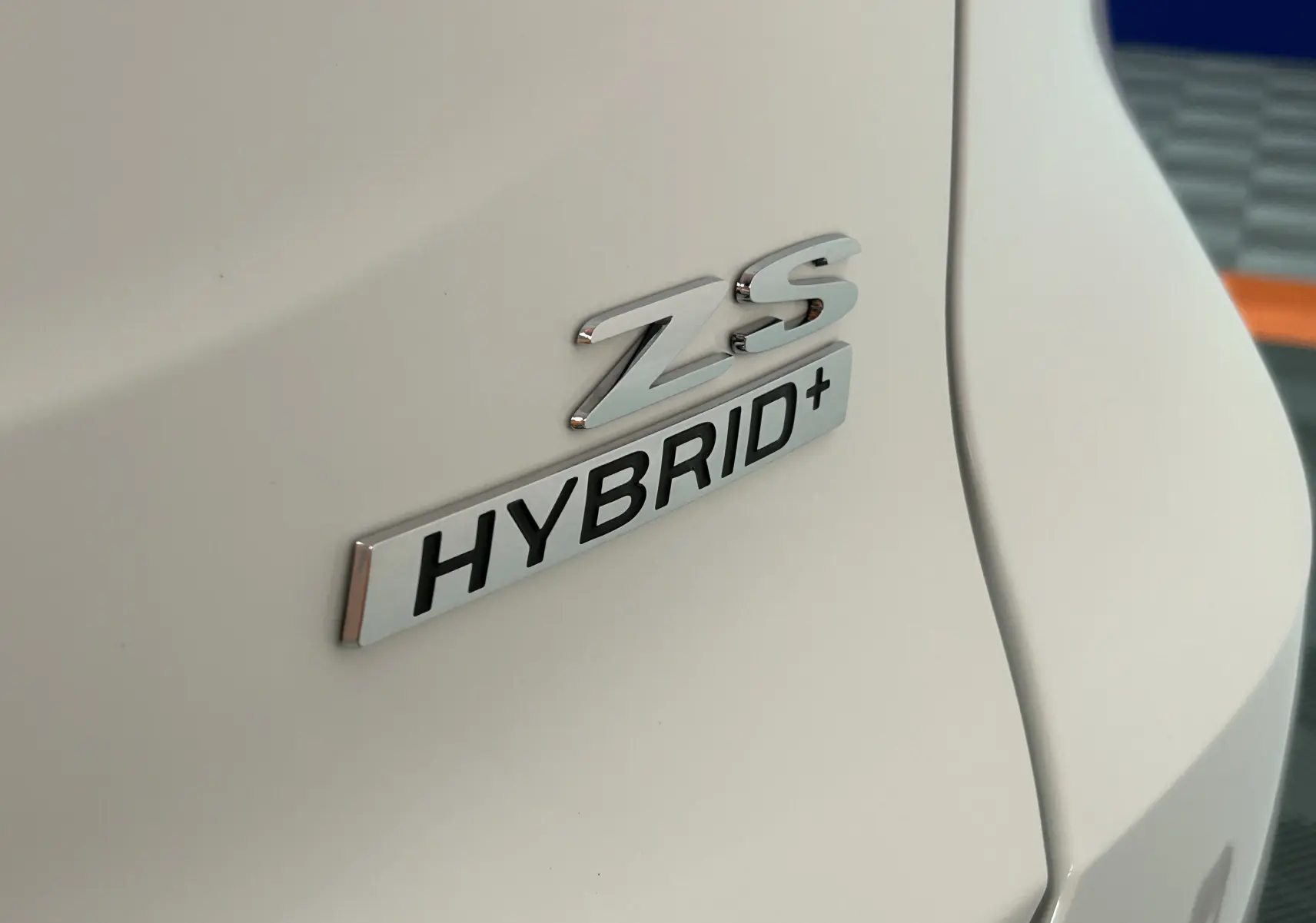 Gros plan sur l’inscription ZS Hybrid+ en chrome sur la carrosserie blanche Dover White d’un MG ZS hybride.