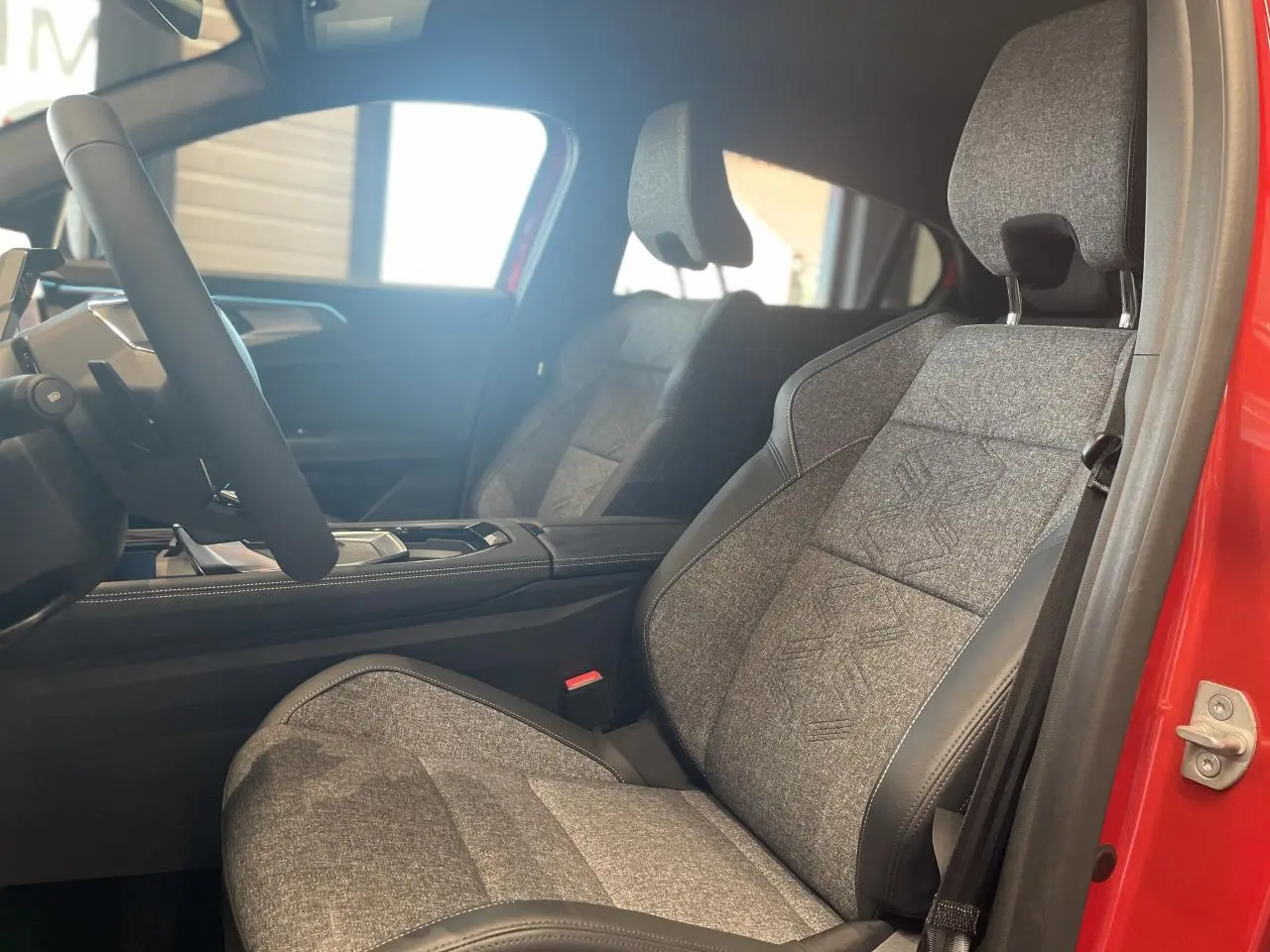 Intérieur côté conducteur du Renault Rafale 2025, siège sport gris textile avec surpiqûres, portière rouge visible.