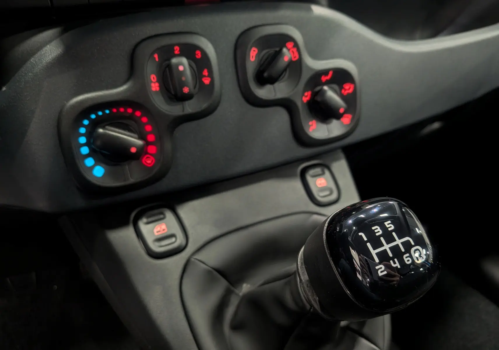 Gros plan sur la commande de la boîte manuelle 6 vitesses et les réglages de climatisation d'une Fiat Panda Bleu Italia 2025.