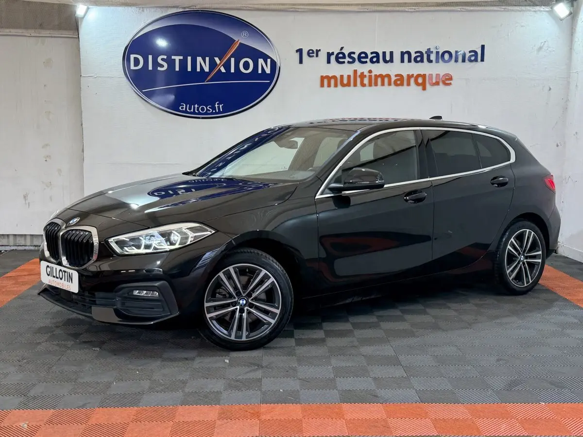 BMW Série 1 116d Business Design noire vue de profil droit en intérieur avec jantes alliage et phares LED allumés.