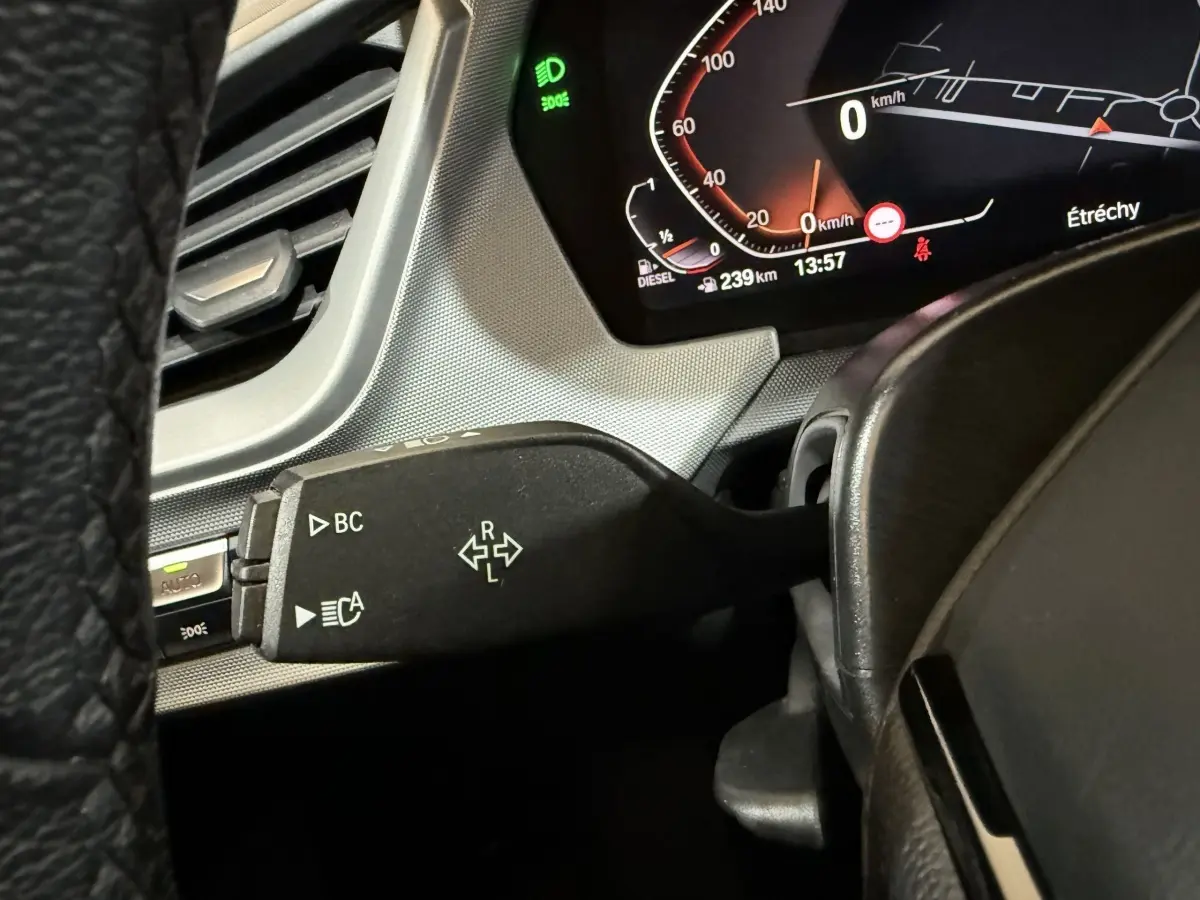 Gros plan sur le commodo gauche du tableau de bord d’une BMW Série 1 116d noir, avec affichage digital et témoin vert allumé.